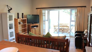 A living room with a wooden TV stand, a television, a dining table with chairs, and a sofa. - Village Lodge Paarl (Paarl)