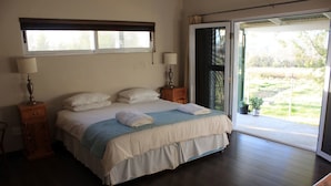 A bedroom with a bed, two bedside tables, a window, and a door leading to a balcony. - Village Lodge Paarl (Paarl)