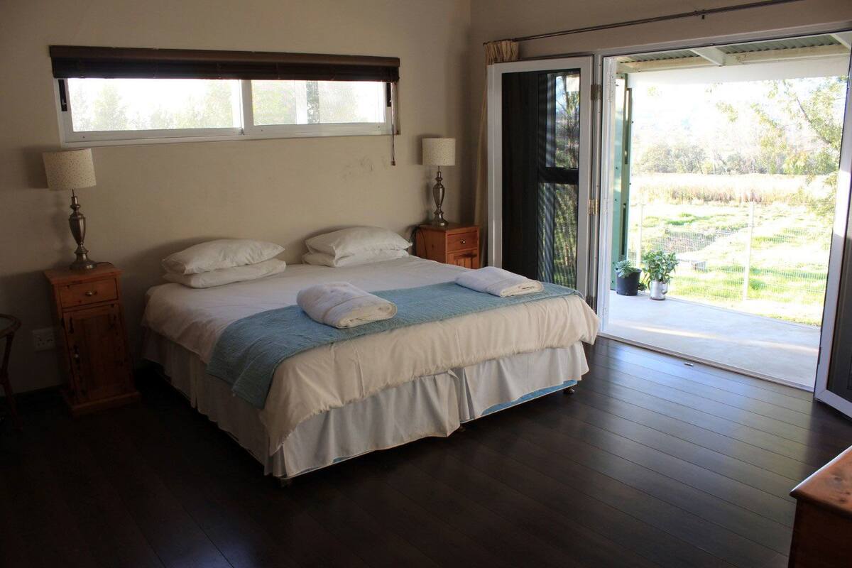 A bedroom with a bed, two bedside tables, a window, and a door leading to a balcony.