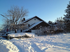 A snow-covered house with a sloped roof and a chimney.