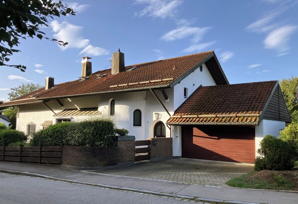 A two-story house with a red-tiled roof, a brick wall, and a wooden gate.