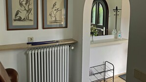 A room with a radiator, a shelf with framed bird illustrations, a mirror with a view of greenery, and a small metal cart. - Absolutely quiet 3 Room Apartment "At Isar River Park",  near Munichs Centre (Grünwald)