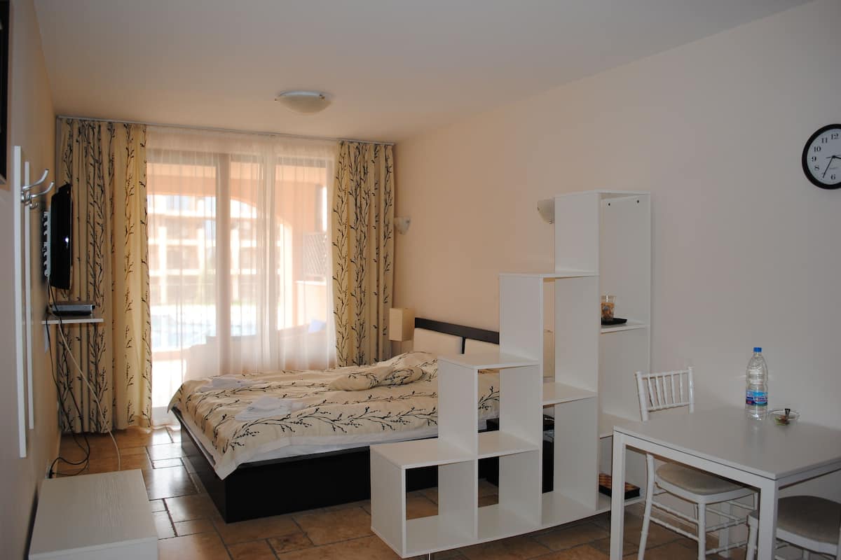 A bedroom with a bed, a desk, a chair, a TV, and a clock on the wall.