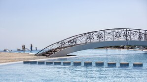 A modern bridge over a pool with a beach in the background. - Kaliakria Resort (Kavarna)