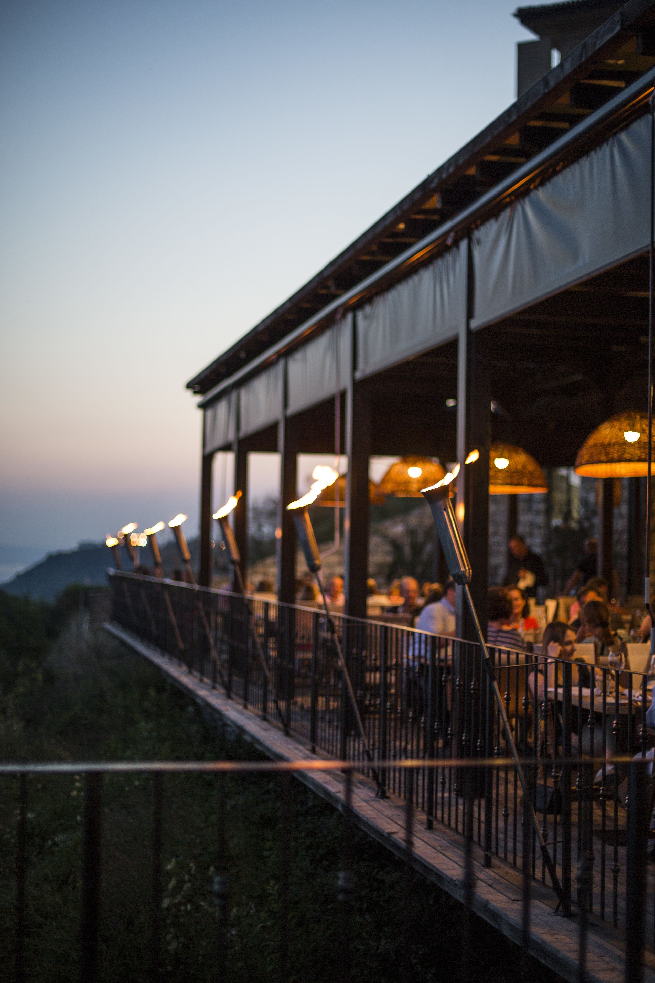 An outdoor dining area with tables and chairs, a railing, and a view of the landscape.