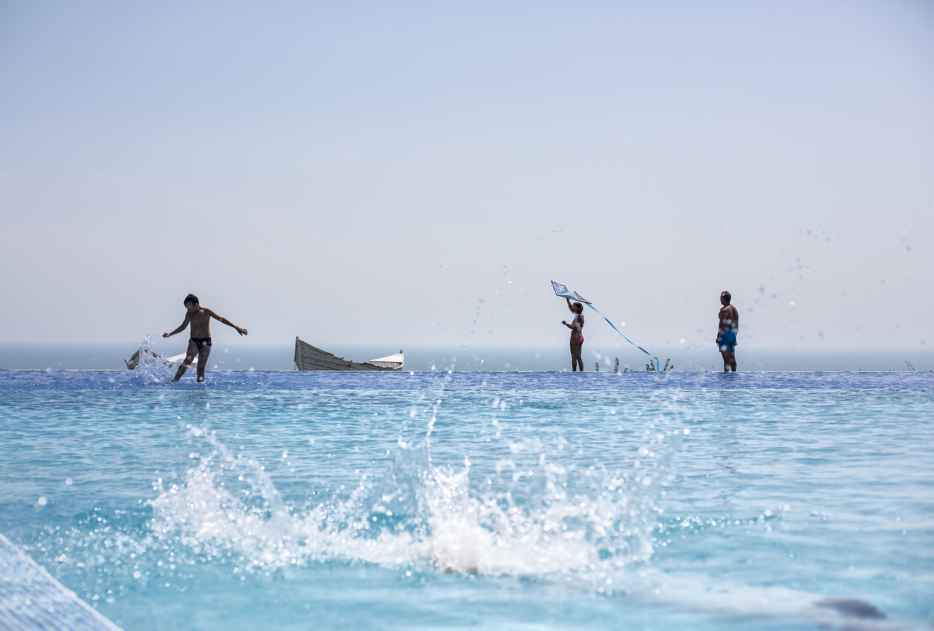 Tres personas en una piscina con un barco al fondo.