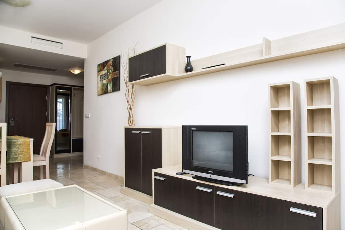 A modern living room with a flat-screen TV, wooden cabinets, and a glass coffee table.