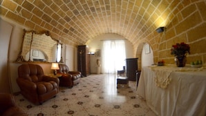 Una habitación amplia con un techo alto abovedado, una chimenea, sillones de cuero, una mesa de comedor con mantel blanco y un espejo en la pared.