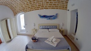 Un dormitorio con una cama grande, dos mesitas de noche, un ventanal y techo de ladrillo.