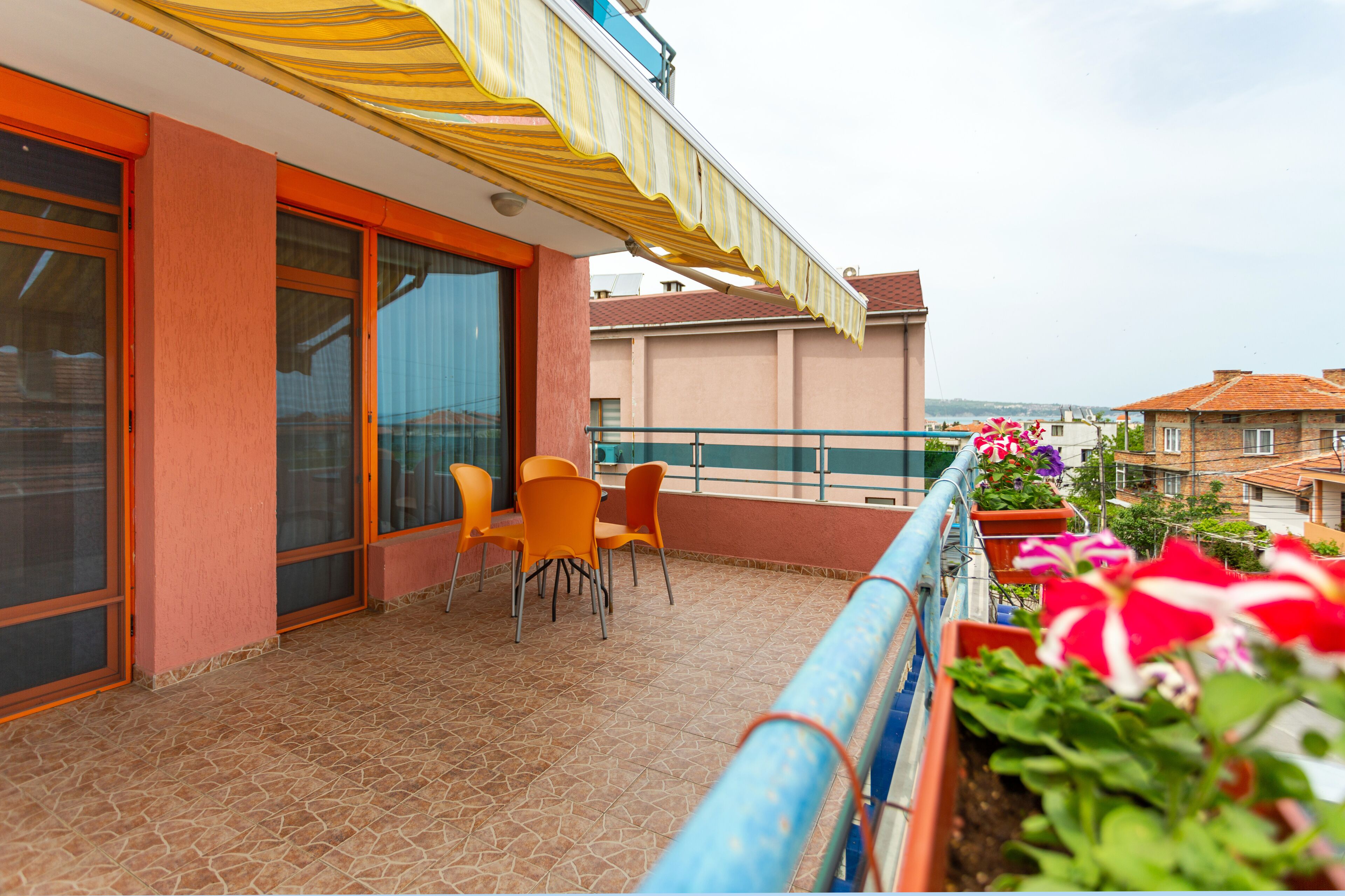 A balcony with orange chairs, a tiled floor, and potted plants.