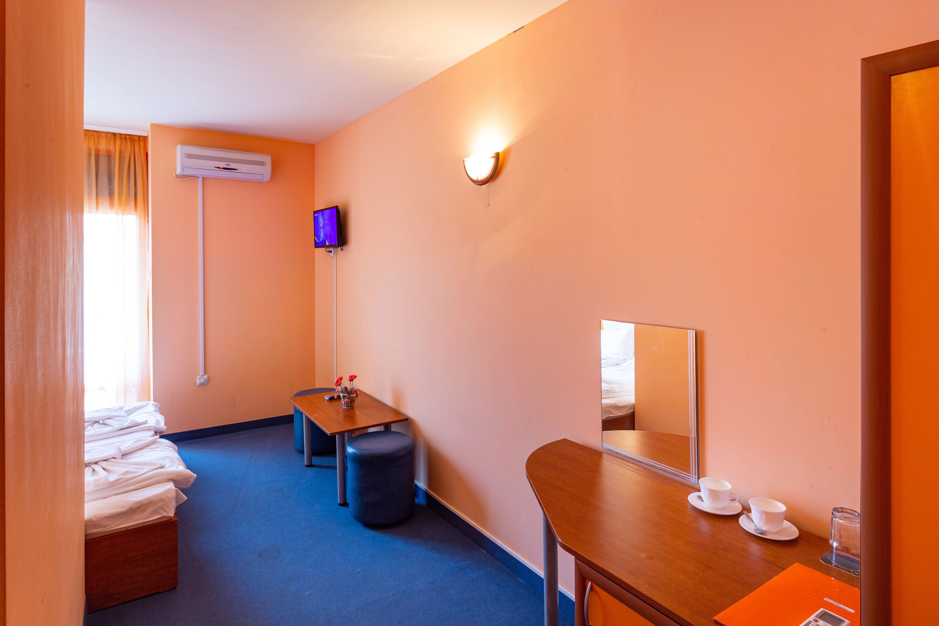 Quarto de hotel com cama, escrivaninha, cadeira, pequena mesa com xícaras, espelho e ar condicionado.