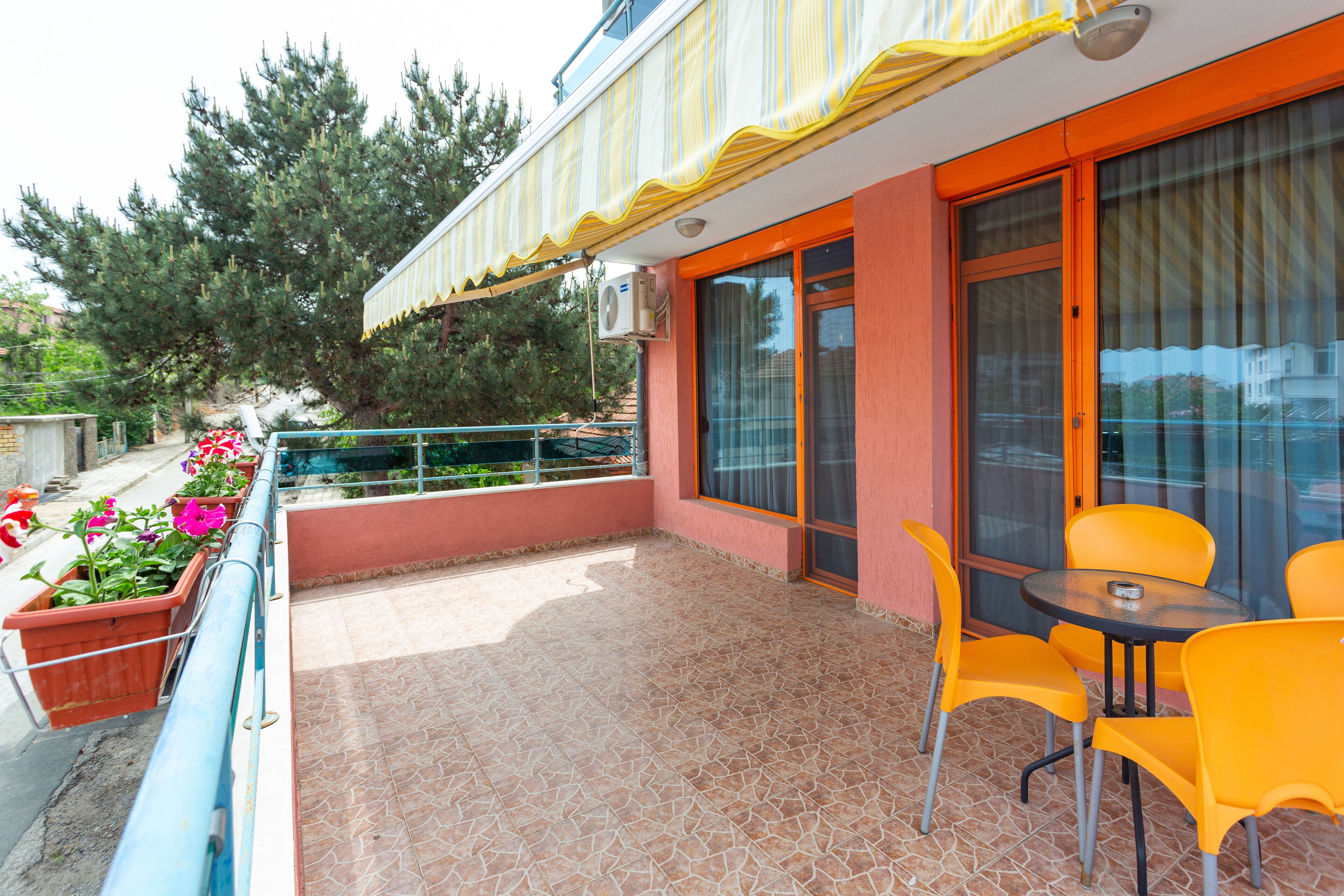 A balcony with yellow chairs and a table, potted plants, and a view of trees.