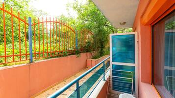 A balcony with a glass railing overlooking a pool and a red fence.