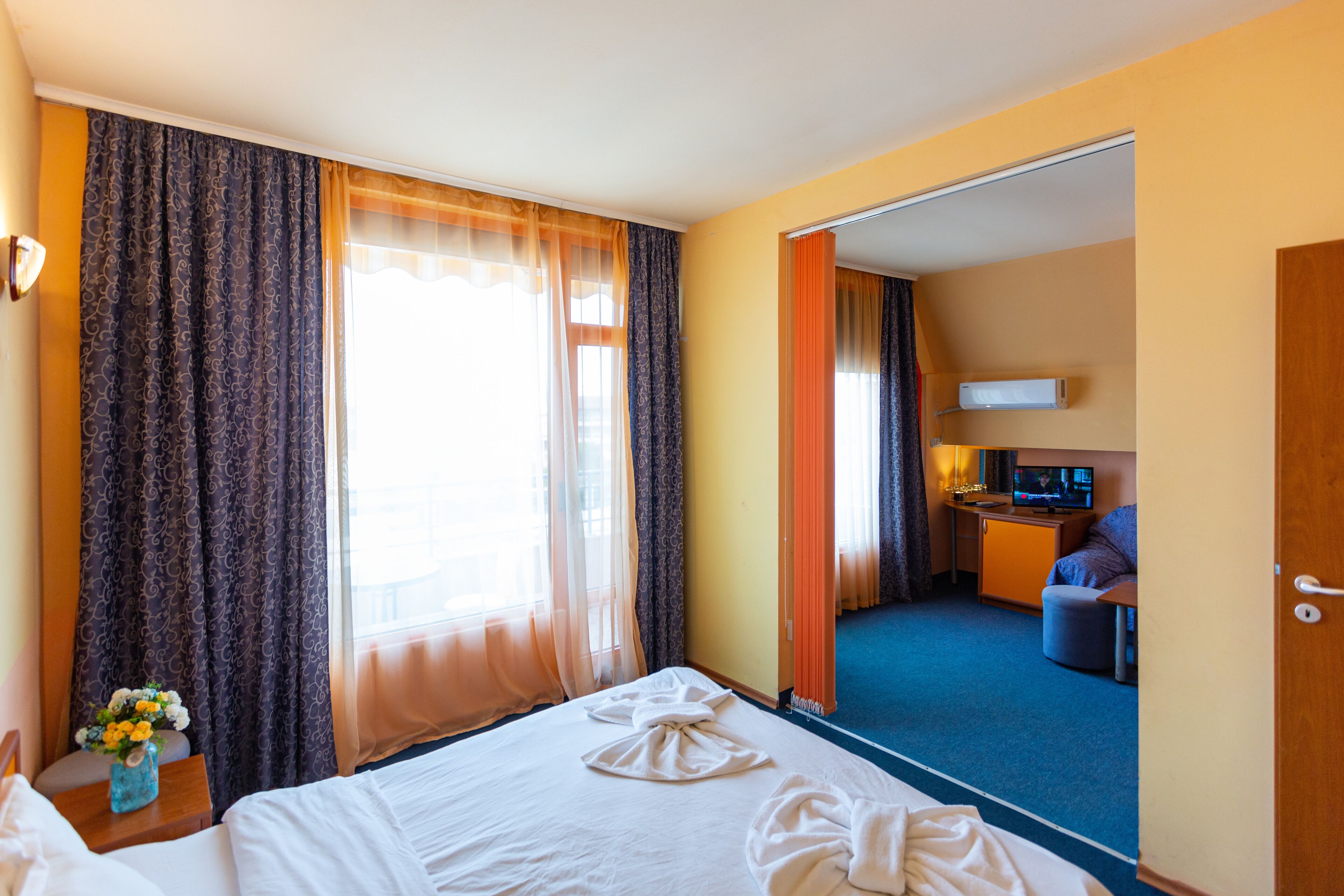 Habitación de hotel con cama, escritorio, televisor y baño visible a través de una puerta abierta.