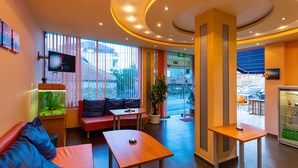 A hotel lobby with seating areas, a television, a fish tank, and a vending machine. - Family Hotel Jemelly (Obzor)