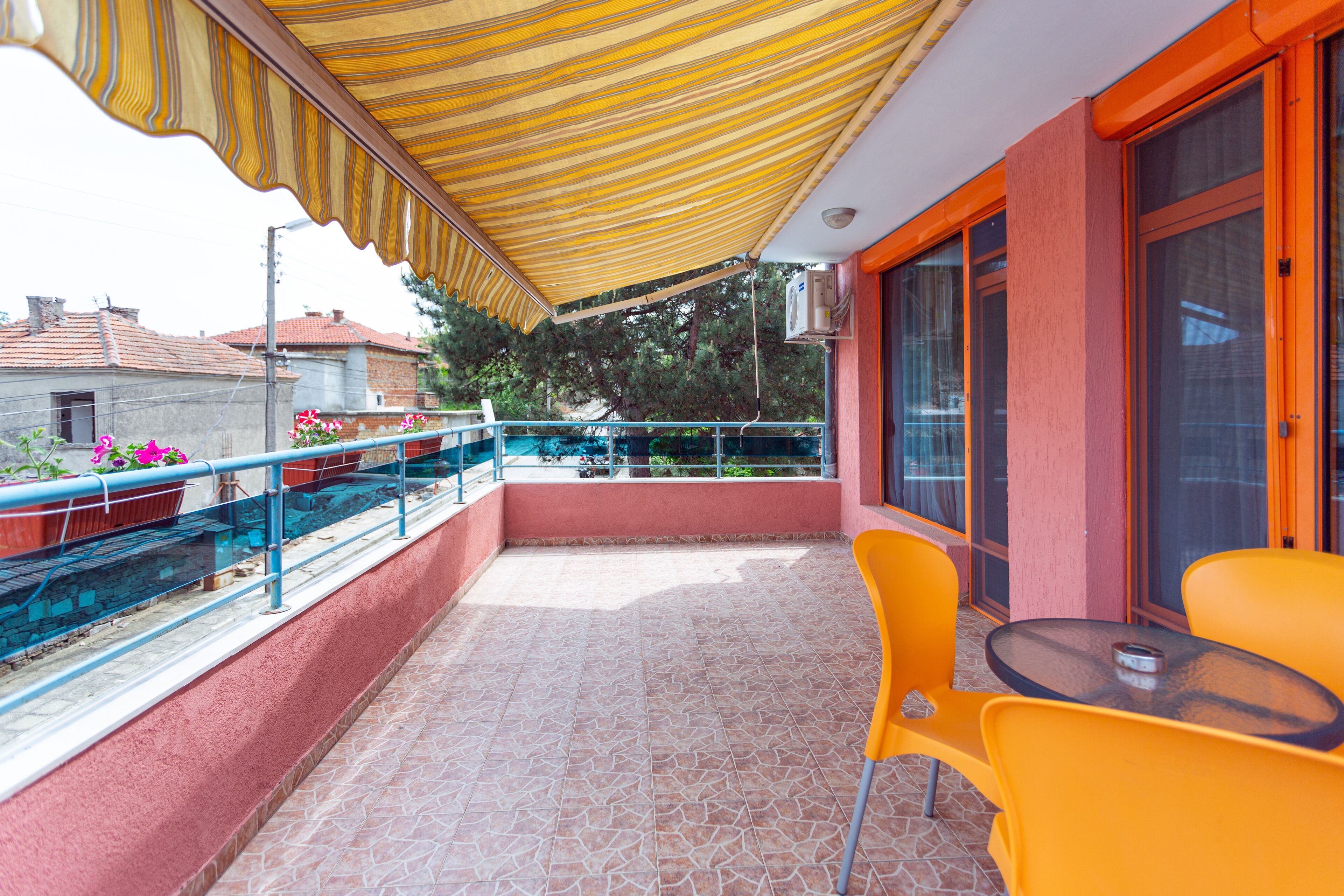 Ein Balkon mit gelbem Streifenverdeck, orangefarbenen Stühlen und einem kleinen Tisch.
