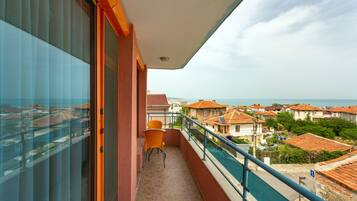 A balcony with a view of a coastal town, a chair, and a tiled floor.