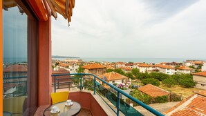 A balcony with a table and chairs, overlooking a coastal town with red-roofed buildings. - Family Hotel Jemelly (Obzor)