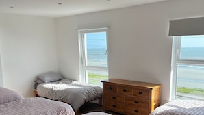 Un dormitorio con dos camas, un aparador de madera y grandes ventanas con vista al mar.