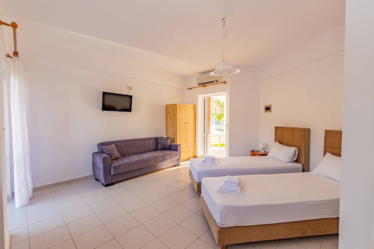 Habitación de hotel con dos camas, un sofá, un televisor y un armario de madera.