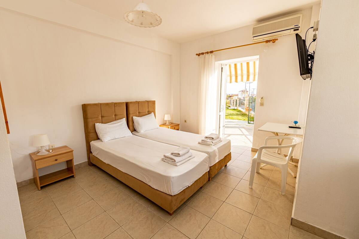 Habitación de hotel con cama doble, mesita de noche con lámpara, una silla y un equipo de aire acondicionado.