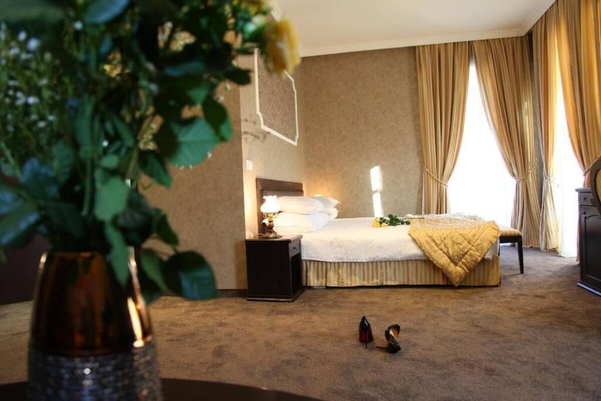 Une chambre d’hôtel avec un lit, une table de chevet, une lampe et une plante au premier plan.