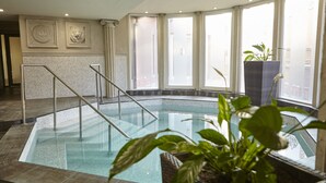 Een binnenzwembad met glazen balustrade, een trap en een potplant.