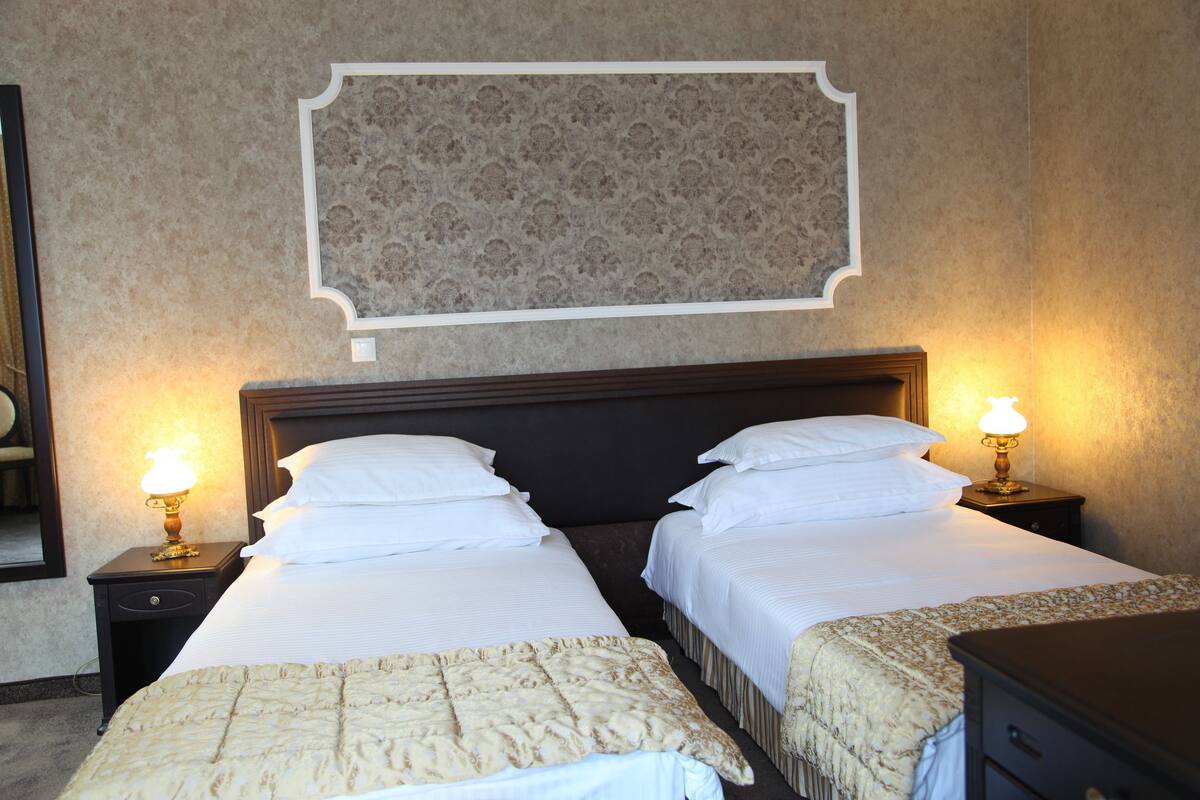 Une chambre d’hôtel avec deux lits, une table de chevet avec une lampe et un miroir au mur.