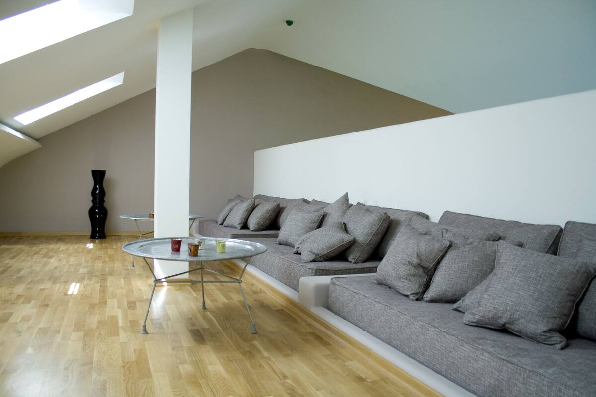 A modern living room with a high ceiling, a grey sofa, a round glass coffee table, and a wooden floor.