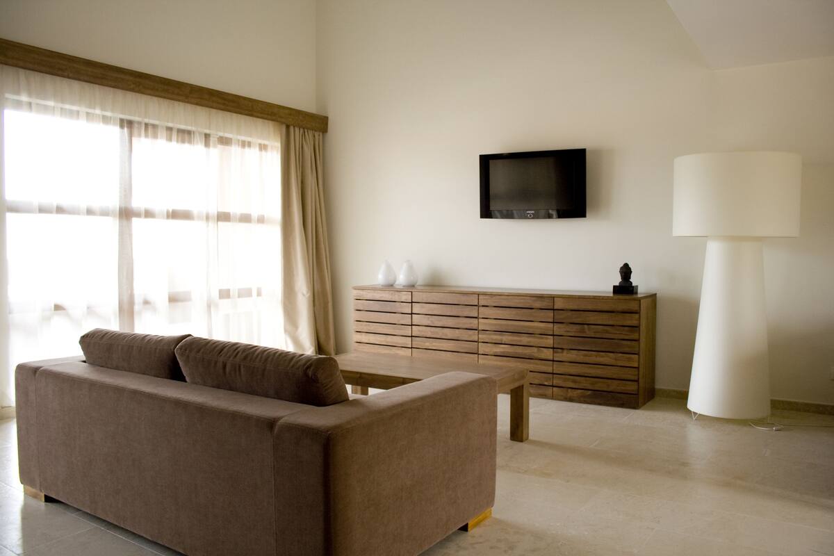 A modern living room with a sofa, a coffee table, a wooden cabinet, a flat-screen TV, and a floor lamp.