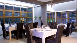 Uma sala de jantar com mesa posta para seis pessoas, rodeada por cadeiras estofadas com design escuro e estampado.