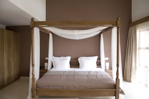 Un letto a baldacchino con lenzuola bianche in una stanza con pavimento in legno e parete marrone.