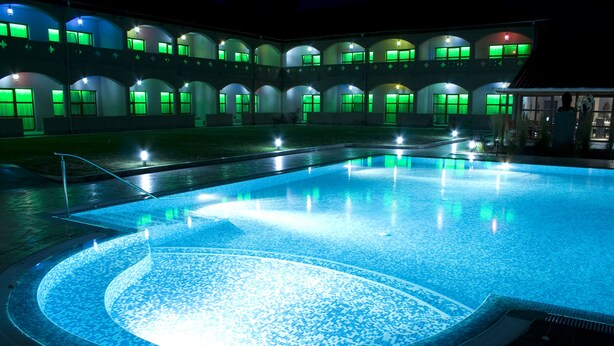 Piscina com borda azulejada e área circular de hidromassagem, cercada por um edifício com várias janelas e arcos.