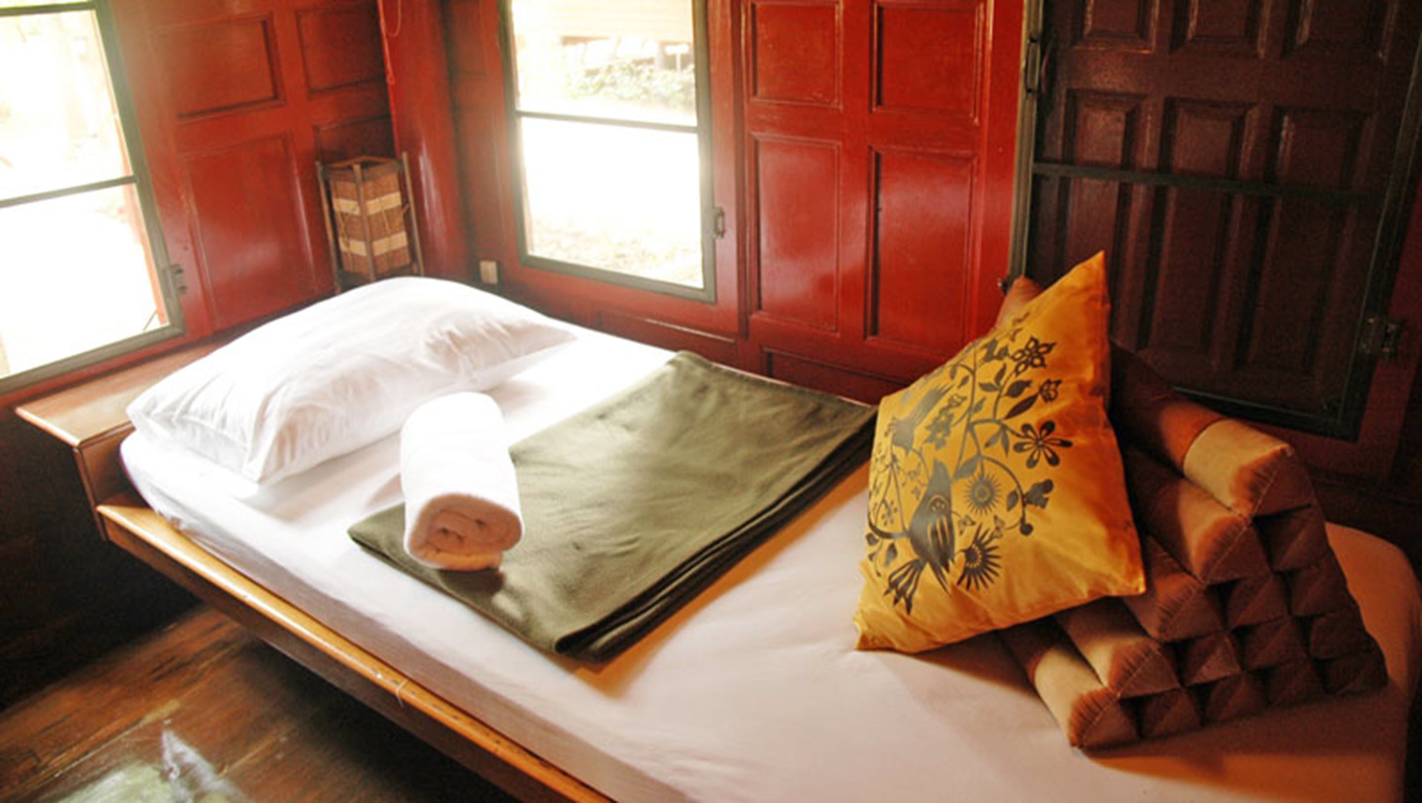 A bed with a white pillow, a rolled-up green blanket, and a decorative yellow pillow.