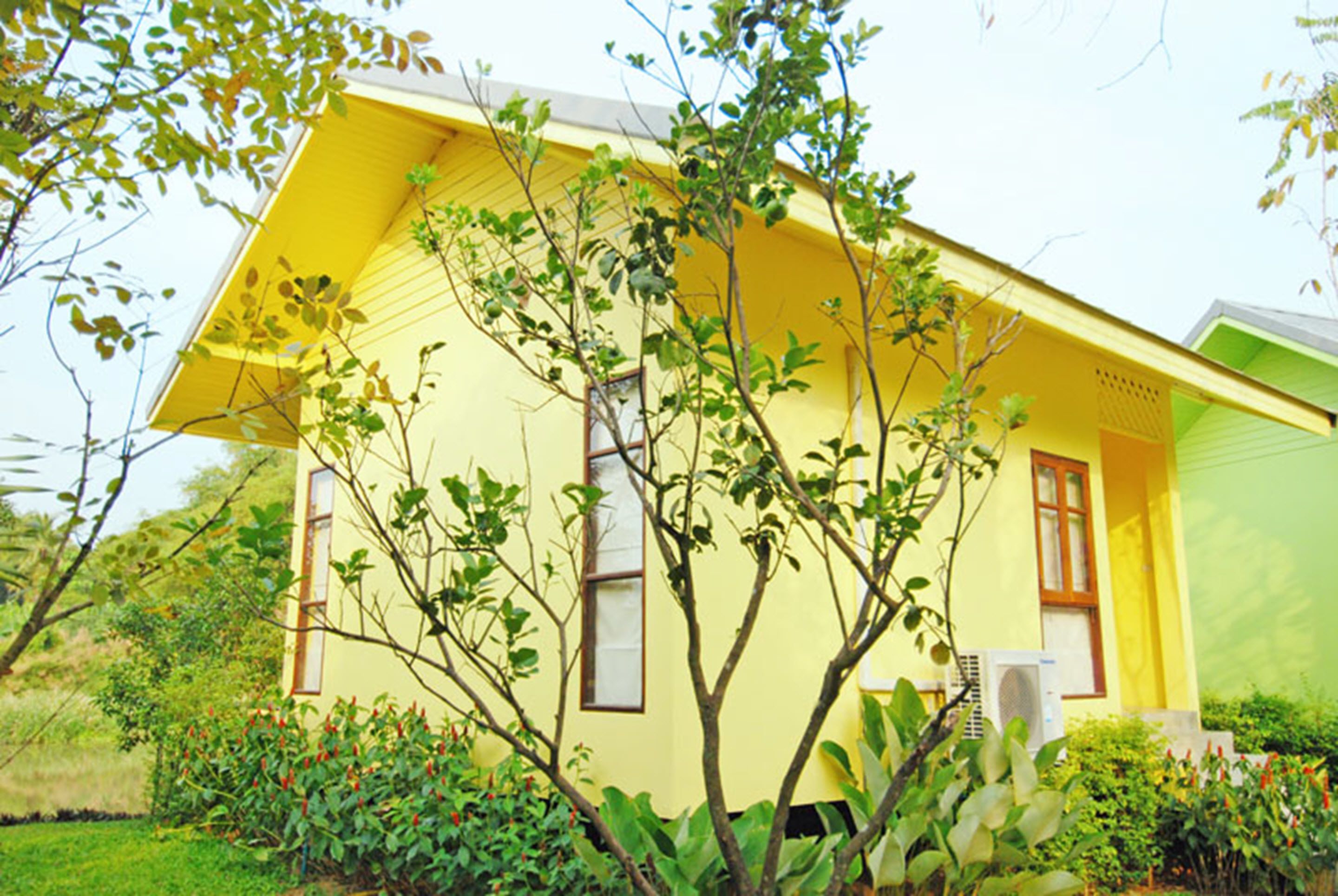 A yellow house with a sloped roof, surrounded by greenery and a small garden.