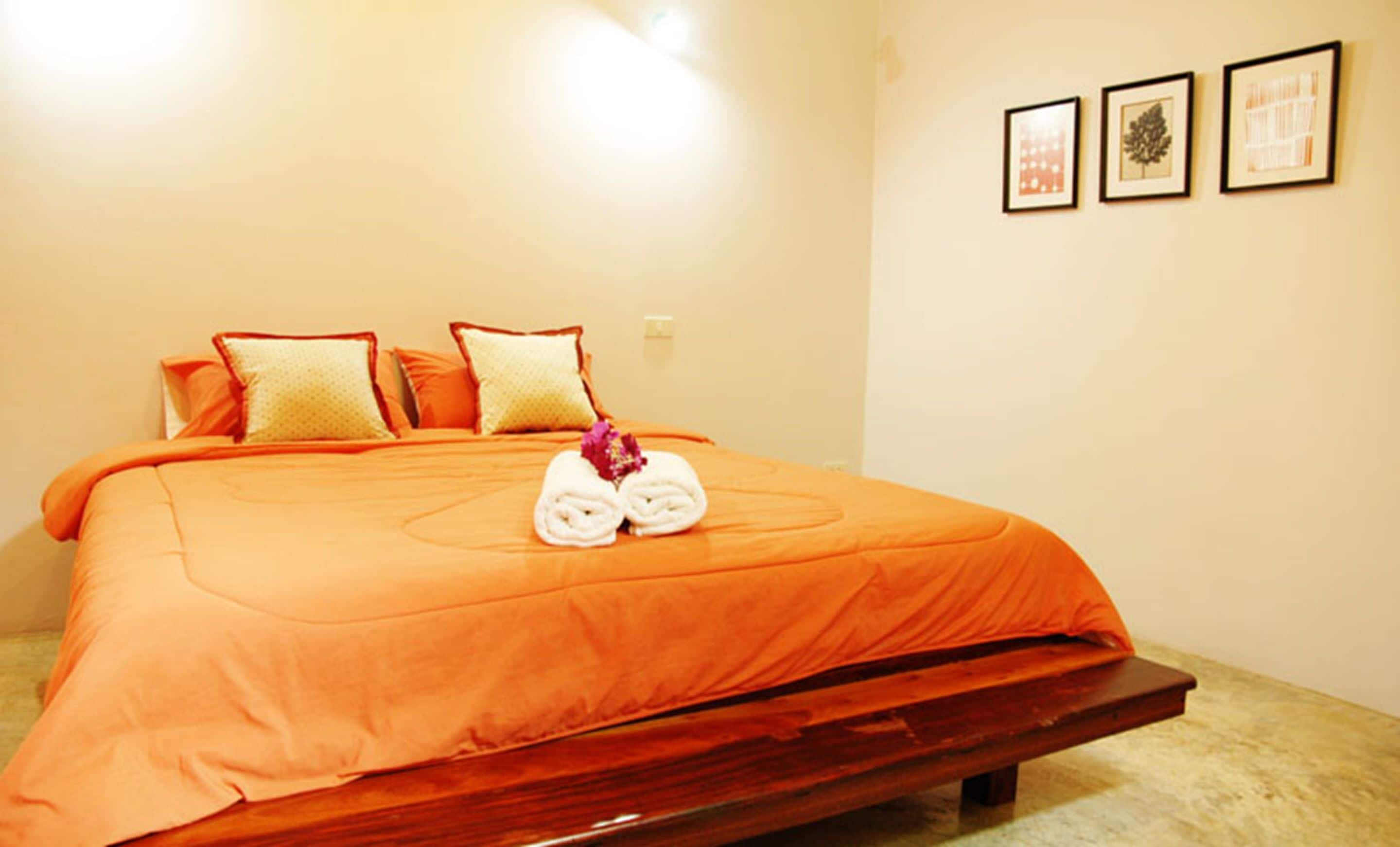 A hotel room with a large bed, orange bedding, and a wooden headboard. There are three framed pictures on the wall.