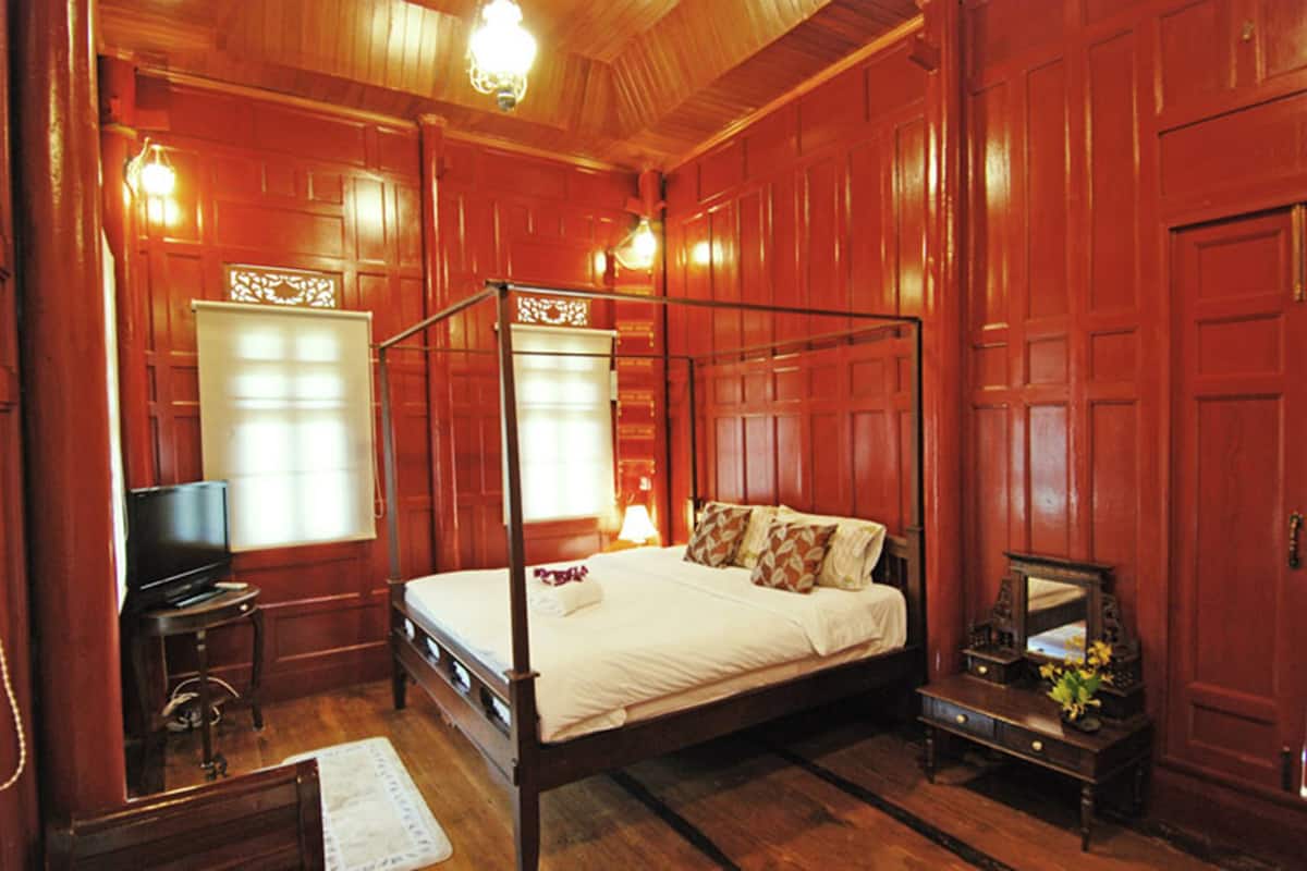 A four-poster bed with a wooden frame, a television on a small table beside it, and a nightstand with a lamp.