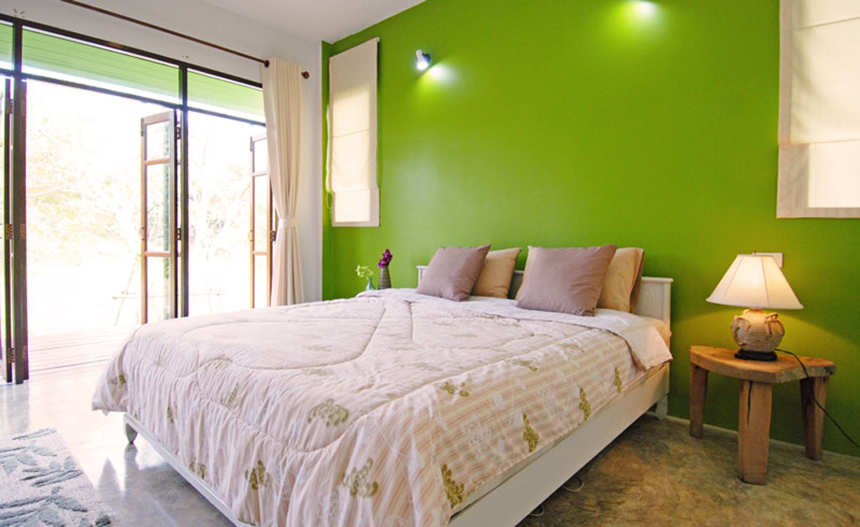 Un dormitorio con una cama grande, una mesita de noche con lámpara y vistas a través de una puerta corrediza de vidrio.