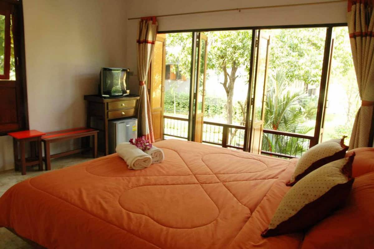 A bedroom with a large bed, a television on a stand, a small table, and a bench.