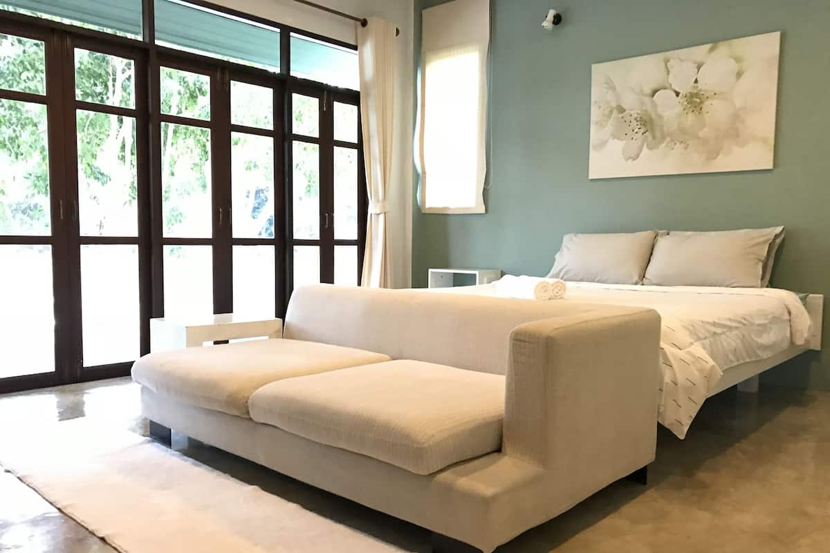 A modern bedroom with a large window, a bed, a sofa, and a wall-mounted artwork.