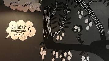 Una pared con diseño de árbol y texto en varios idiomas dando la bienvenida a visitantes en Doembangvilla.