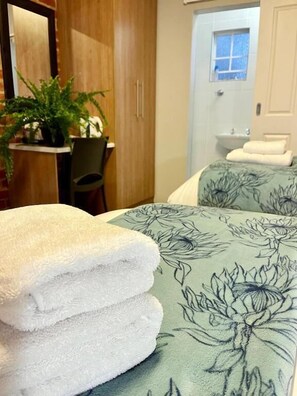 A hotel room with a bed, a bedside table with a plant, a chair, and a bathroom visible through an open door.