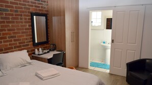 Une chambre d’hôtel avec un lit, un bureau, une chaise, un miroir et une salle de bain visible à travers une porte ouverte.