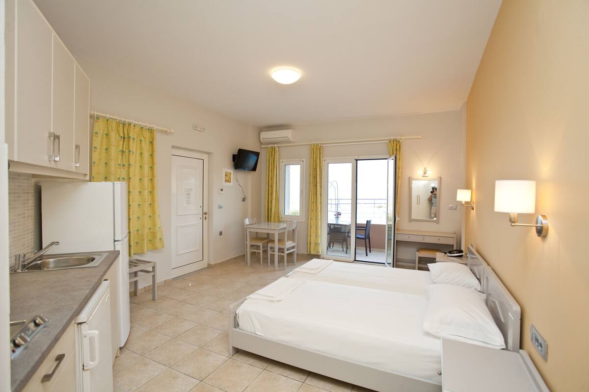 Habitación de hotel con cama, escritorio, silla, kitchenette pequeño y baño.