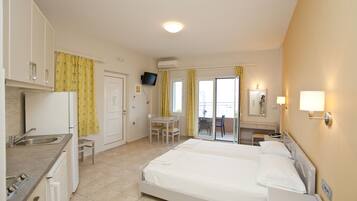 A hotel room with a bed, a desk, a chair, a small kitchenette, and a bathroom.