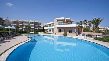 A swimming pool with lounge chairs and umbrellas, surrounded by modern buildings and palm trees.