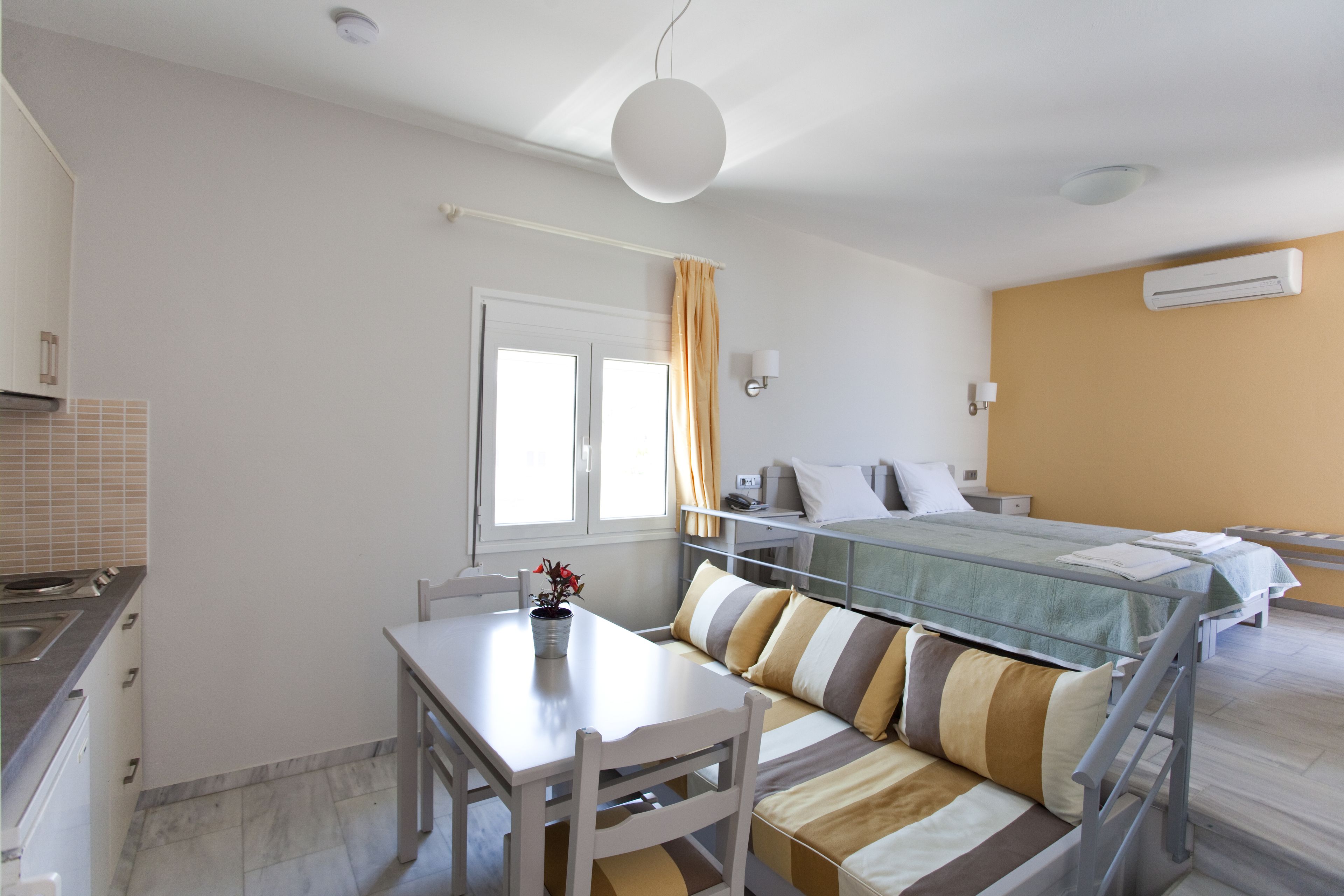 A bedroom with a bed, a bedside table, a chair, a window with curtains, and an air conditioning unit.