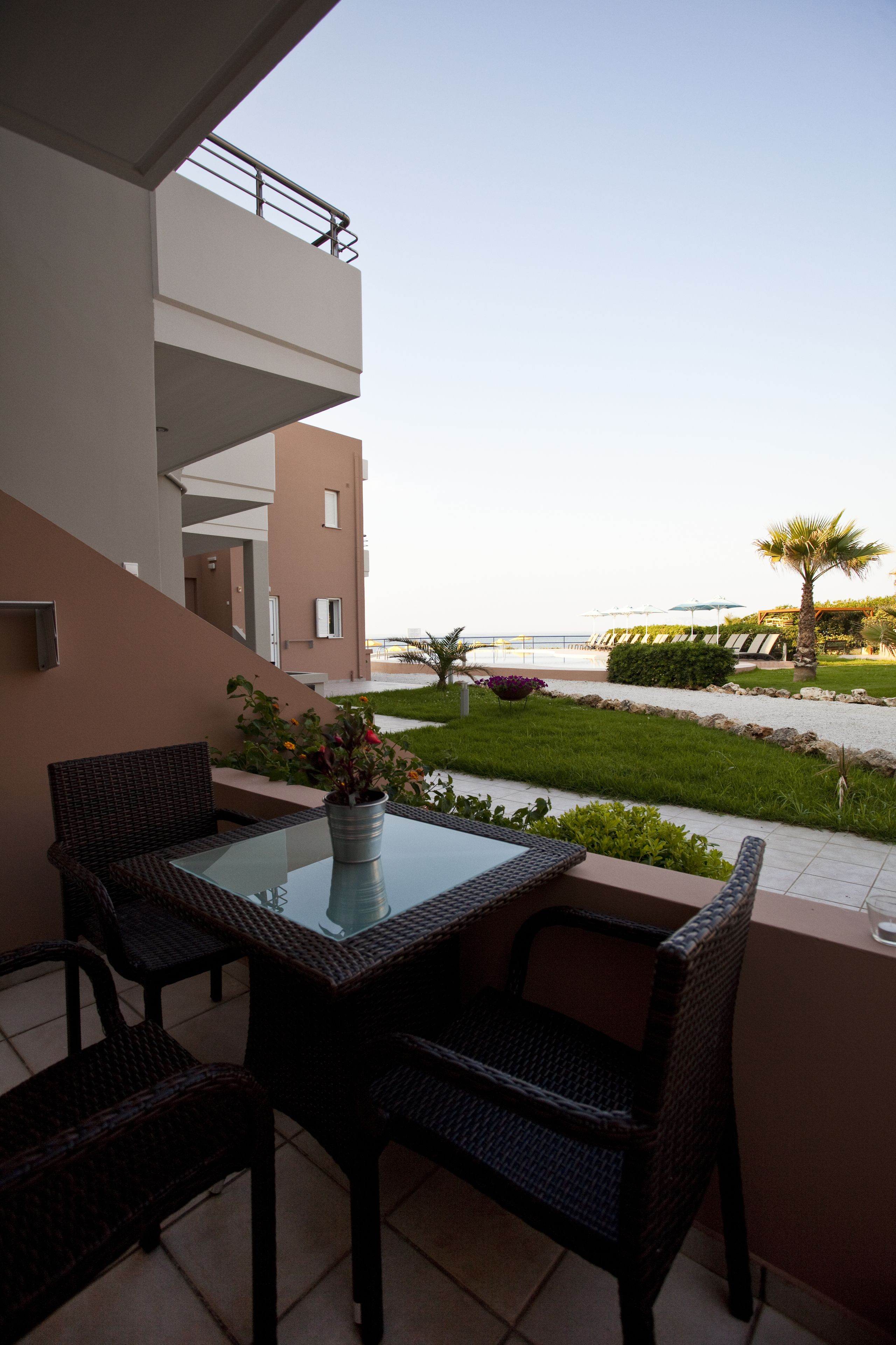 A balcony with wicker furniture, a glass table, and a potted plant.