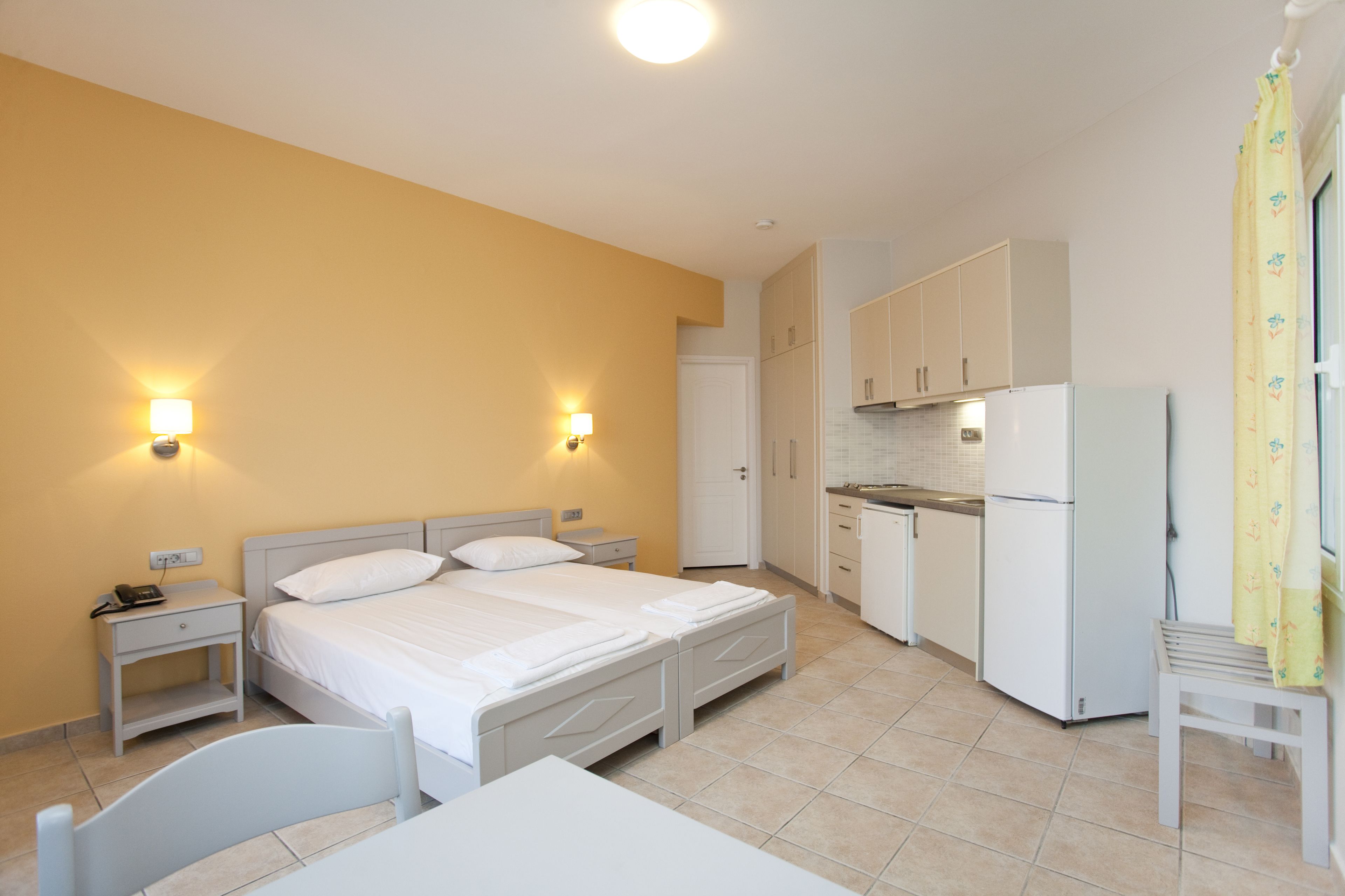 Una habitación compacta con una cama individual, mesitas de noche y una pequeña kitchenette.