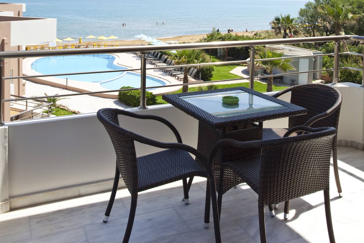 Un balcón con vista al mar, una piscina y mobiliario exterior.